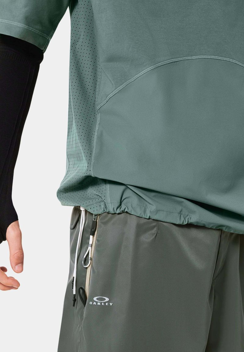 T-shirt de sport vert clair avec des panneaux en mesh et un ourlet élastique, associé à un short gris avec cordon de serrage et détail de logo.