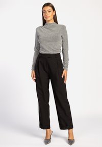 Grijze langemouwen top met een hoge hals, gecombineerd met zwarte wijde broek met studs. Model draagt puntige hakken.