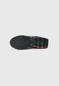 Black running shoe sole with textured grip, featuring green accents and red circular details. Robust design with a thick profile.
