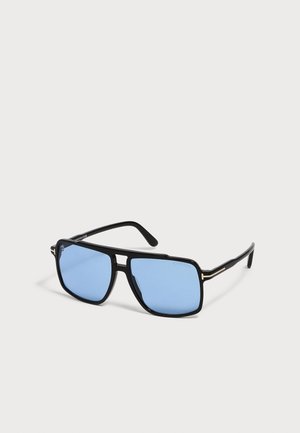 Lunettes de soleil à monture noire avec verres rectangulaires teintés en bleu et branches fines, exposées sur une surface claire.