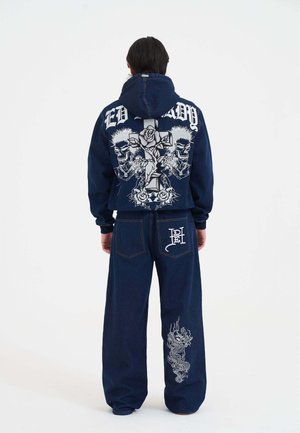 Sudadera de mezclilla azul oscuro y pantalones de pierna ancha. La sudadera presenta un gran diseño gráfico con calaveras y rosas; los pantalones tienen un intrincado bordado de dragón.