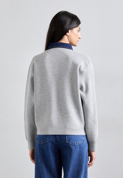 Maglione grigio con scollatura rotonda, maniche a costine e colletto in denim. Indossato con jeans blu a vita alta, che mostrano una vestibilità rilassata.