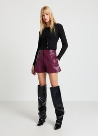 Haut noir à manches longues côtelé, ajusté avec fermeture à boutons. Short en fausse cuir bordeaux, taille haute. Bottes noires jusqu'aux genoux, à bouts pointus.