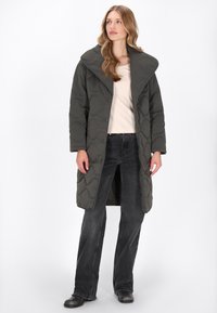 Sötét szürke puffernadrág nagy gallérral, textúrázott steppelt mintázattal és patentos záródással, világos felsőre és sötét farmernadrágra véve.