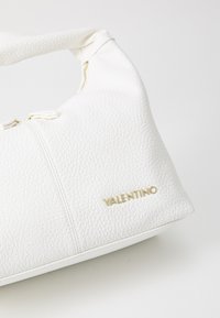 White leather handbag with a textured finish, curved shape, gold hardware, and embossed "Valentino" logo. Zipper accent at the top.