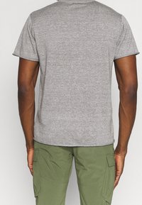 Grå t-shirt med kort ärm och rund halsringning. Slät textur och avslappnad passform, parat med olivgröna cargo-byxor med sidofickor.