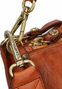 Hoek van een bruine leren handtas met een gestructureerd oppervlak, gouden hardware, een ritsluiting en een haak voor het bevestigen van een schouderband.