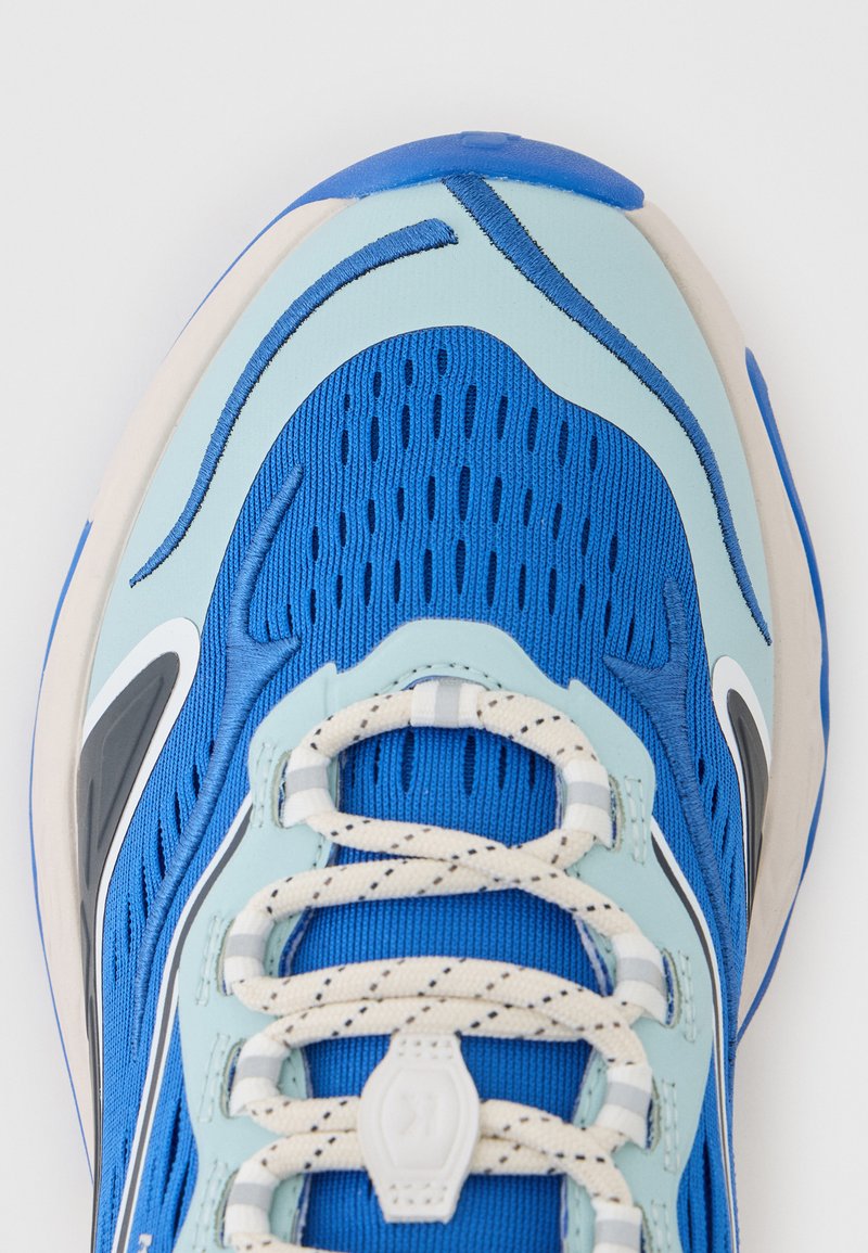 Zapatilla deportiva azul y azul claro con cordones blancos y grises, parte superior de malla y suela de goma, vista desde arriba.