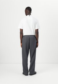 Cămașă albă cu mâneci scurte, cu un accent negru la guler, asociată cu pantaloni gri care au un buzunar posterior, textură netedă și croială lejeră.