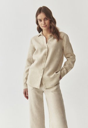 Light beige linen shirt with a button-down front and collar, paired with matching loose-fitting linen pants. Subtle texture visible.