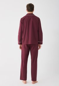 Burgundy pyžamový set s dlouhým rukávem, který zahrnuje košili na knoflíky a odpovídající kalhoty, s bílými lemy kolem límce a manžet, vyrobený z měkkého materiálu.