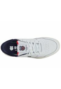 White sneaker with perforated toe, textured navy blue collar, red and navy accents, and K-Swiss logo on tongue. Features flat grey laces.