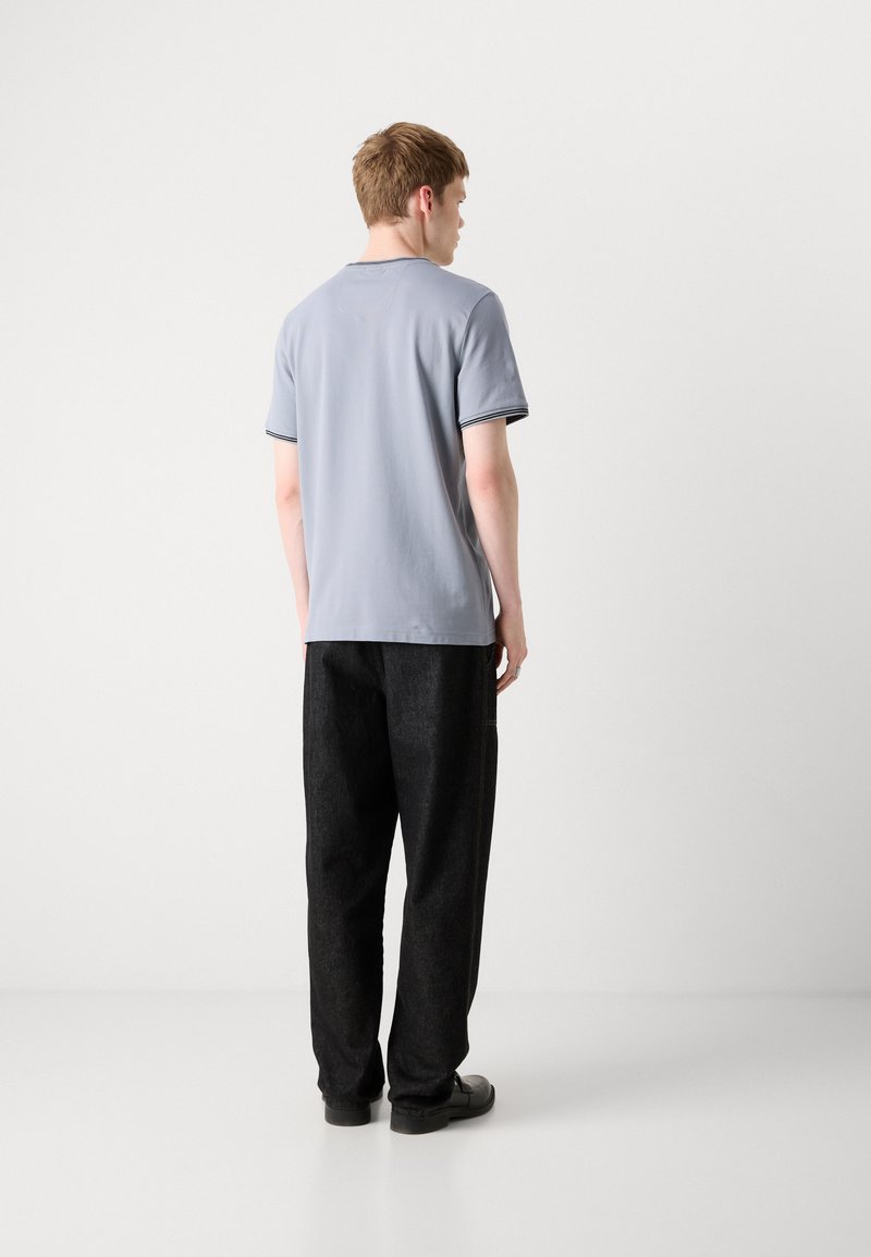 T-shirt à manches courtes gris avec des accents rayés bleu marine, associé à un pantalon noir ample et des chaussures noires. Design simple et décontracté.