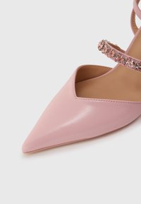 Ροζ δερμάτινο παπούτσι με μυτερή μύτη, σχέδιο με κοψίματα και διακοσμητικό λουράκι με λαμπερά στρας. Λεία υφή με ματ φινίρισμα.