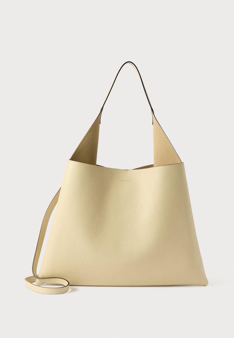 Läderhandväska i ljusgul med slät struktur. Har en minimalistisk design, öppen topp och lång axelrem.