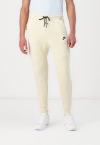 Helle beigefarbene Nike Jogginghosen mit slim fit, schmal zulaufenden Beinen, verstellbarem Kordelzugbund, Seitentaschen und schwarzem Logo-Detail.