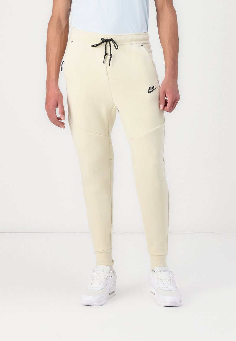Helle beigefarbene Nike Jogginghosen mit slim fit, schmal zulaufenden Beinen, verstellbarem Kordelzugbund, Seitentaschen und schwarzem Logo-Detail.