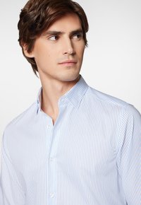 Koszula zapinana na guziki w niebiesko-białe pionowe paski, wykonana z bawełny, z kołnierzykiem typu wykładany i dopasowanym krojem.