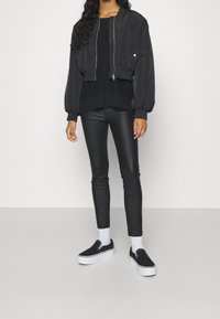 Blouson aviateur noir au design court, associé à un pantalon noir ajusté et des baskets plates noires avec semelles blanches.