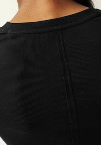 Top in tessuto nero a coste con scollatura rotonda e dettagli cuciti. La texture appare liscia, evidenziando il design aderente.