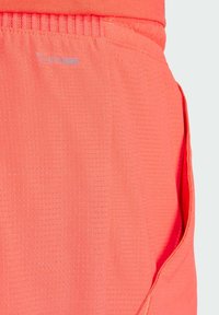 Climalite shorts in bright coral, featuring a textured fabric with horizontal lines and a side pocket for convenience.