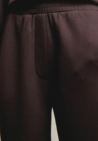Donkerbruine joggingsbroek met een zachte structuur, voorzien van een elastische tailleband en een discret zijzakje. Eenvoudig, gestroomlijnd ontwerp.