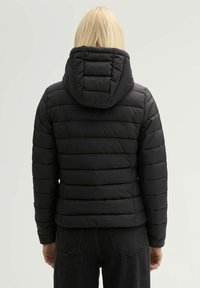 Zwarte pufferjack met horizontaal gestikte ontwerpen, afneembare capuchon en een gladde textuur. Kenmerken zijn elastische manchetten en een getailleerd silhouet.