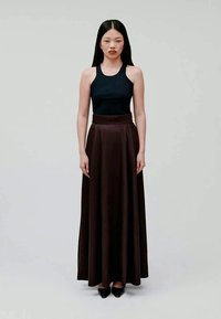 Schwarzes Tanktop und langer, dunkelbrauner Rock. Glattes Material mit fließender, A-Linie-Form, kombiniert mit spitzen, schwarzen Schuhen. Einfaches, elegantes Design.