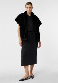 Zwarte nepbont sjaal over een zwarte, geribbelde midi-jurk met subtiele glinsterende accenten, gecombineerd met zwarte platte schoenen.