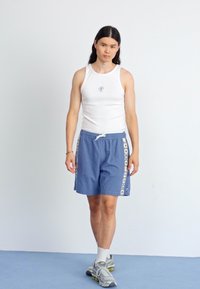Hvit tanktopp med rund hals; blå shorts med mønstrede sidelommer; grå joggesko. Enkelt design, uformell atletisk stil.