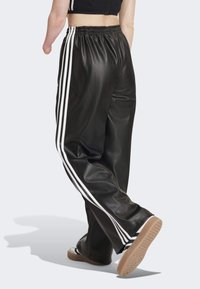 Svarta byxor i konstläder med vita sidostråk, elastisk midja och lös passform. Utrustade med en strukturerad yta och avslappnade sneakers.