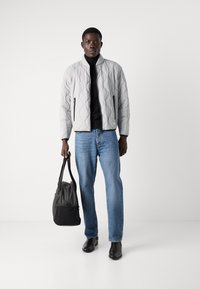 Light gray quilted bomber jacket with a black turtleneck, blue jeans, and black boots, holding a dark gray bag with a long strap.