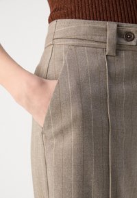 Bruna randiga byxor med rak passform, texturerat tyg, sidoficka och knappstängning i midjan.