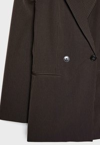 Blazer marrone a righe con design doppiopetto, dotato di due bottoni neri e un dettaglio a tasca singola. Tessuto liscio e texture.