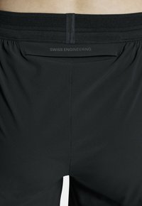 Zwarte sportshorts met een ademende mesh tailleband, voorzien van kleine perforaties en de tekst "SWISS ENGINEERING" op de achterkant.