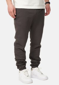 Schwarze Jogginghosen mit elastischen Bündchen, seitlichen Taschen und einer glatten Textur, kombiniert mit weißen Sneakers. Einfaches, funktionales Design.