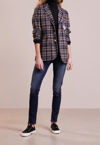 Navy kariertes Blazer mit taillierter Passform, einfacher Knopfverschluss und zwei Vorderaschen, kombiniert mit dunklen Jeans und schwarzen Sneakers.