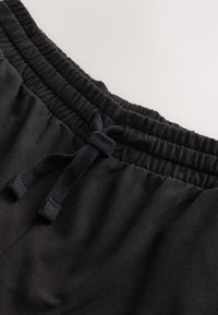 Pantalones cortos deportivos negros con cintura elástica y cordón de ajuste. Textura de tela suave; sin patrones ni adornos visibles.