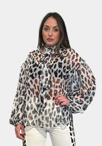 Blusa trasparente con stampa leopardata marrone e nera su sfondo bianco, con maniche a sbuffo e dettaglio del colletto annodato.