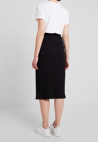 Jupe midi noire à côtes avec un design ajusté, fente sur le côté et texture lisse, associée à des baskets blanches pour un look décontracté.