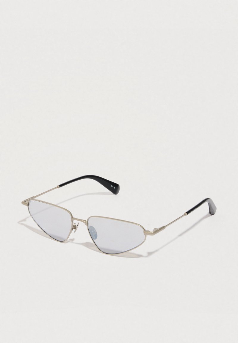 Óculos de sol com armação prateada, hastes pretas finas e lentes angulares em formato de gato ligeiramente coloridas, sobre uma superfície branca.