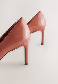 Sjajne ružičaste cipele od lakirane kože s visokom potpeticom, s dizajnom šiljastog vrha, elegantnog oblika i tankom štiklom na petu.