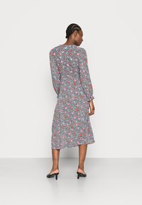 Vestido floral com mangas compridas, base preta, flores vermelhas e azuis, tecido leve, com comprimento médio, apresenta punhos franzidos, usado com saltos pretos.