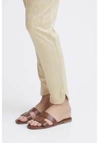 Jasno beżowe spodnie w panterkę z bocznymi rozcięciami, zestawione z brązowymi, płaskimi sandałami z dwoma szerokimi paskami i dekoracyjną klamrą.