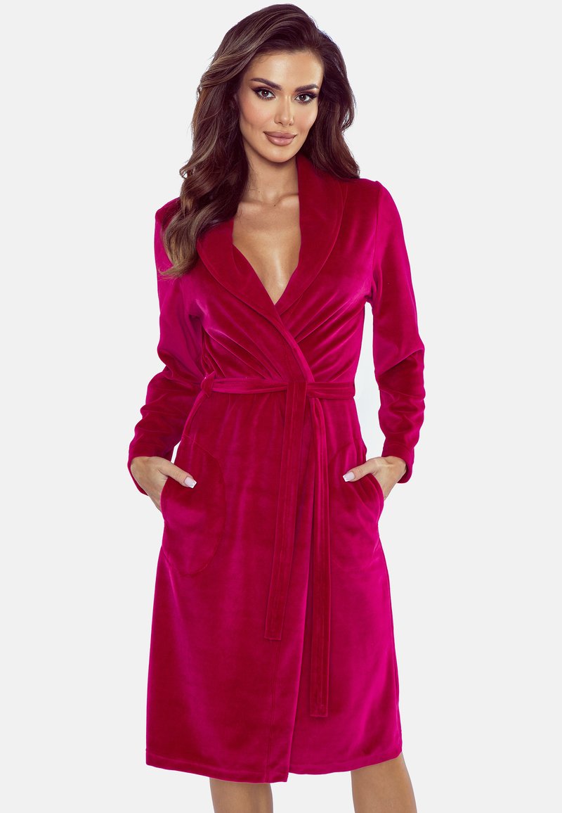 Roba in velluto fucsia con colletto a scialle, maniche lunghe, vita con lacci e due tasche frontali; morbida texture e design fino al ginocchio.