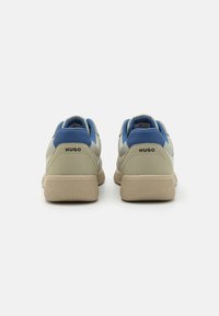 Baskets pour hommes en cuir beige et bleu, dotées d'une semelle en caoutchouc texturé et du logo "HUGO" à l'arrière. Design arrondi avec une apparence superposée.