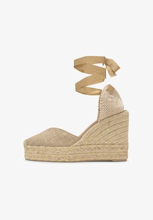 Espadrillas beige con zeppa in corda intrecciata, cinturino alla caviglia con fiocco, tomaia chiusa e testata del tallone decorata.