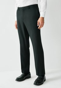 Czarne dopasowane spodnie o gładkiej fakturze, proste nogawki i szlufki na pasek, w połączeniu z czarnymi mokasynami i białą koszulą. 