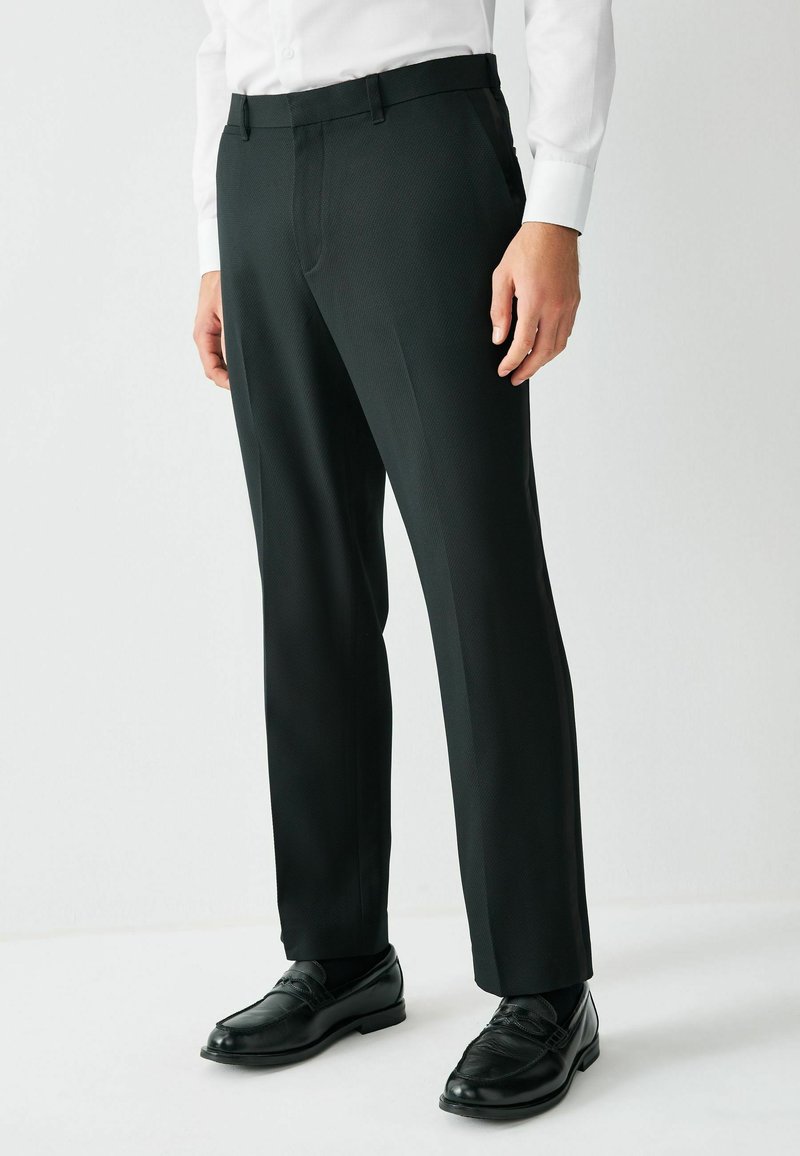 Czarne dopasowane spodnie o gładkiej fakturze, proste nogawki i szlufki na pasek, w połączeniu z czarnymi mokasynami i białą koszulą. 