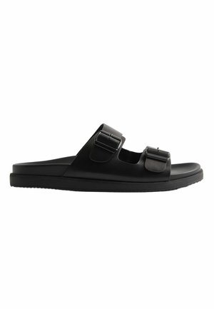 Sort slip-in sandal med to justerbare remme med spænder og flad sål, designet til afslappet brug.